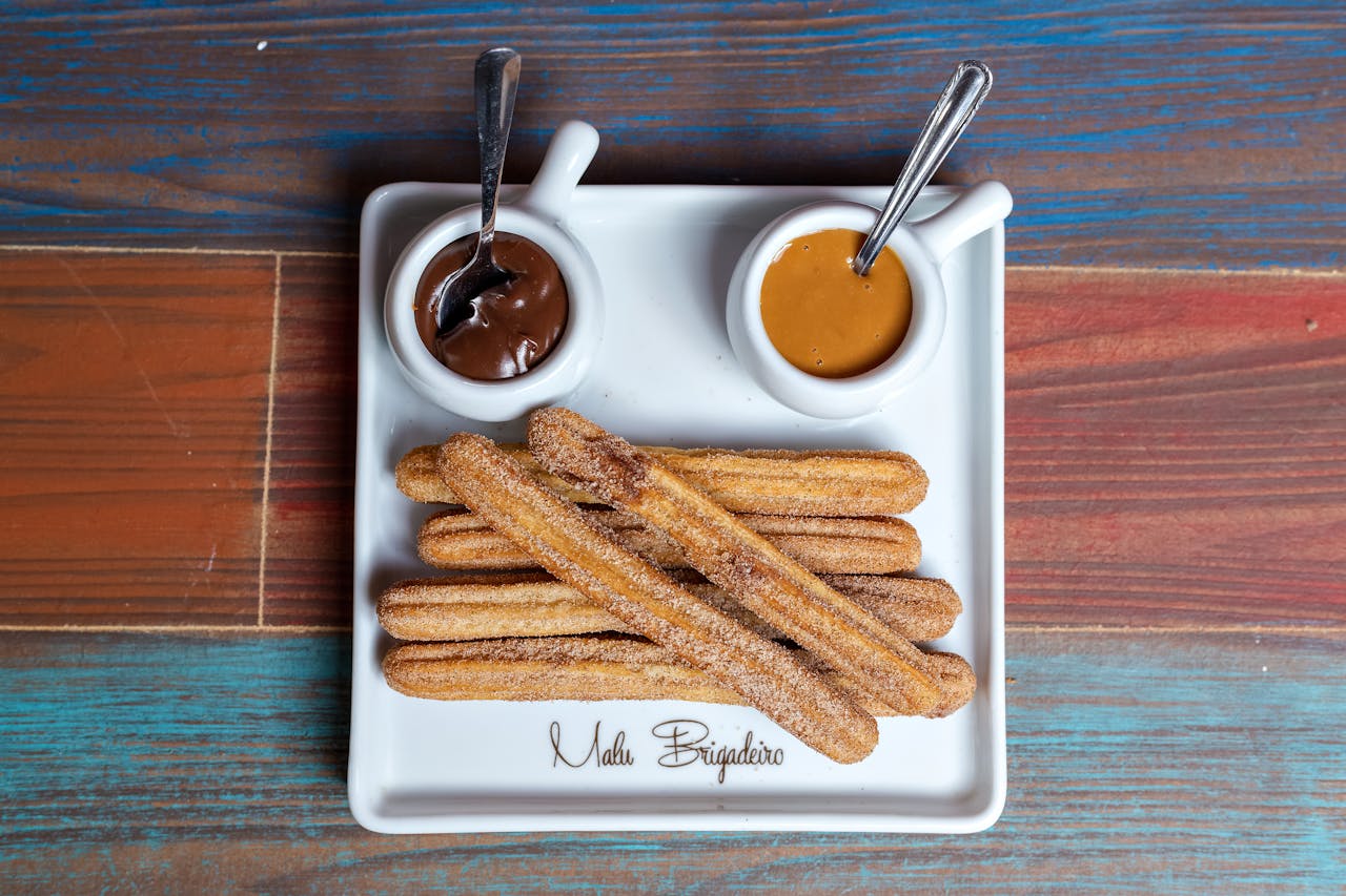 Sweet churros served with chocolate and caramel dips on a rustic wooden table.