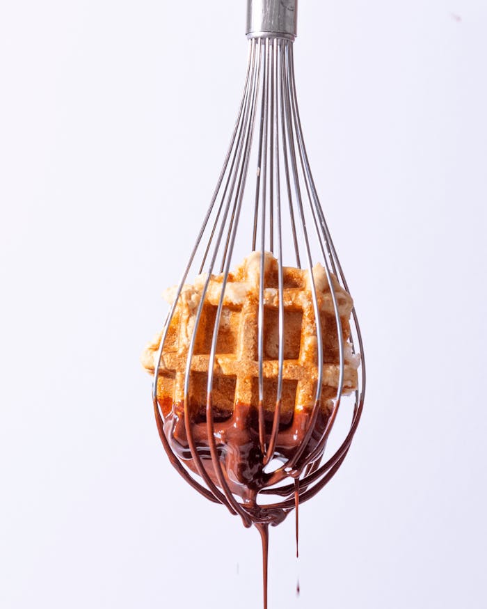 Mouth-watering waffle dipped in rich chocolate hanging from a whisk. Perfect for dessert inspiration.